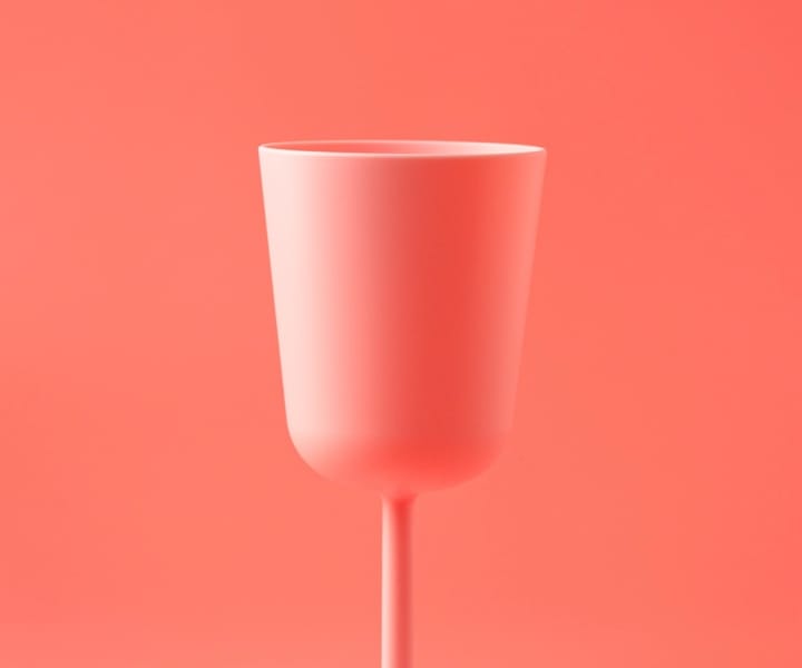 A pink plastic wine glass with a pink background